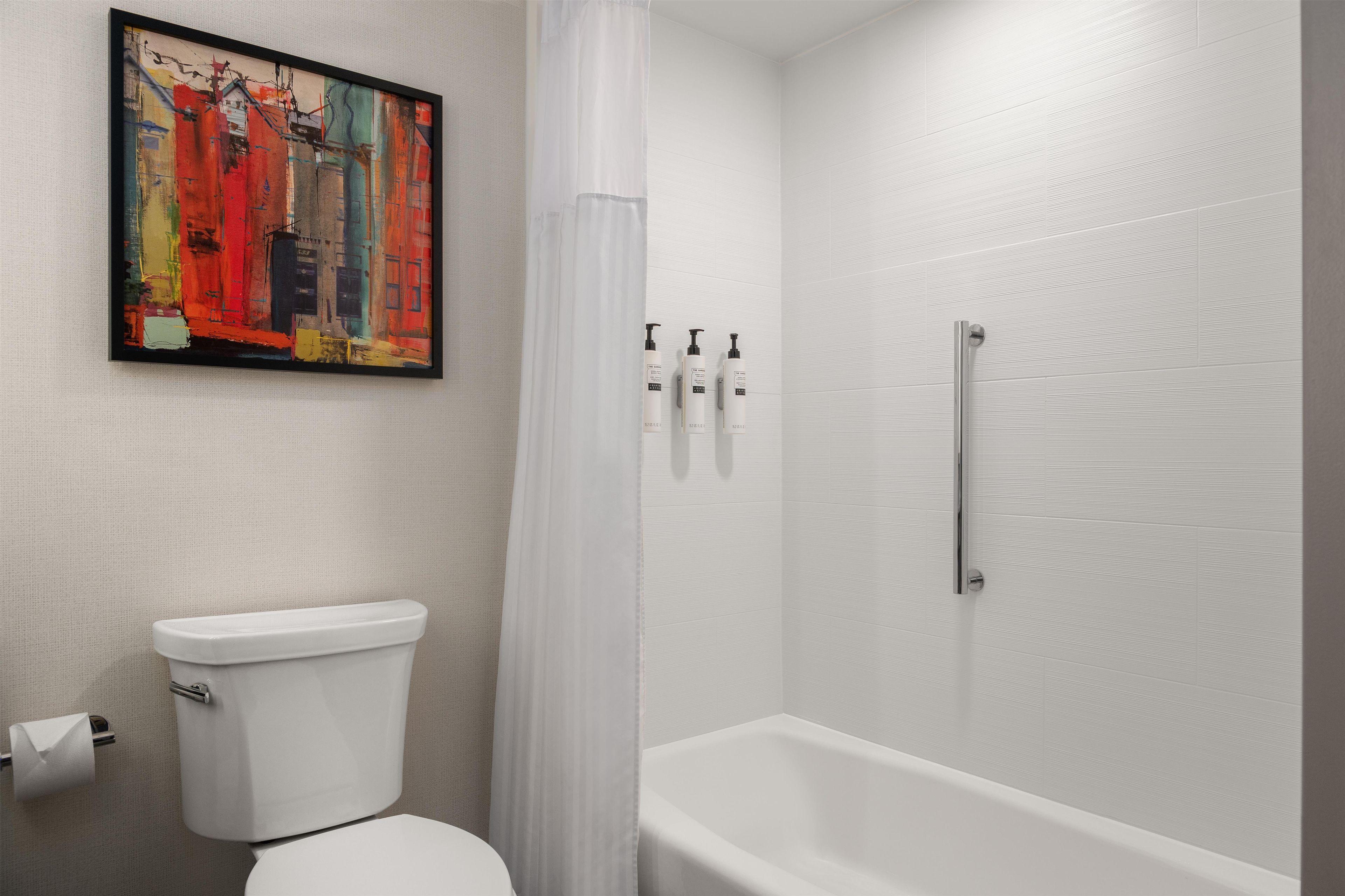 A bathroom with a toilet, a shower with a glass door, and a framed abstract painting on the wall.