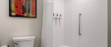 A bathroom with a toilet, a shower with a glass door, and a framed abstract painting on the wall.