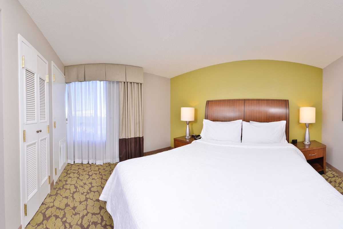 A hotel room with a large bed, two bedside tables with lamps, a television, and a framed picture on the wall.