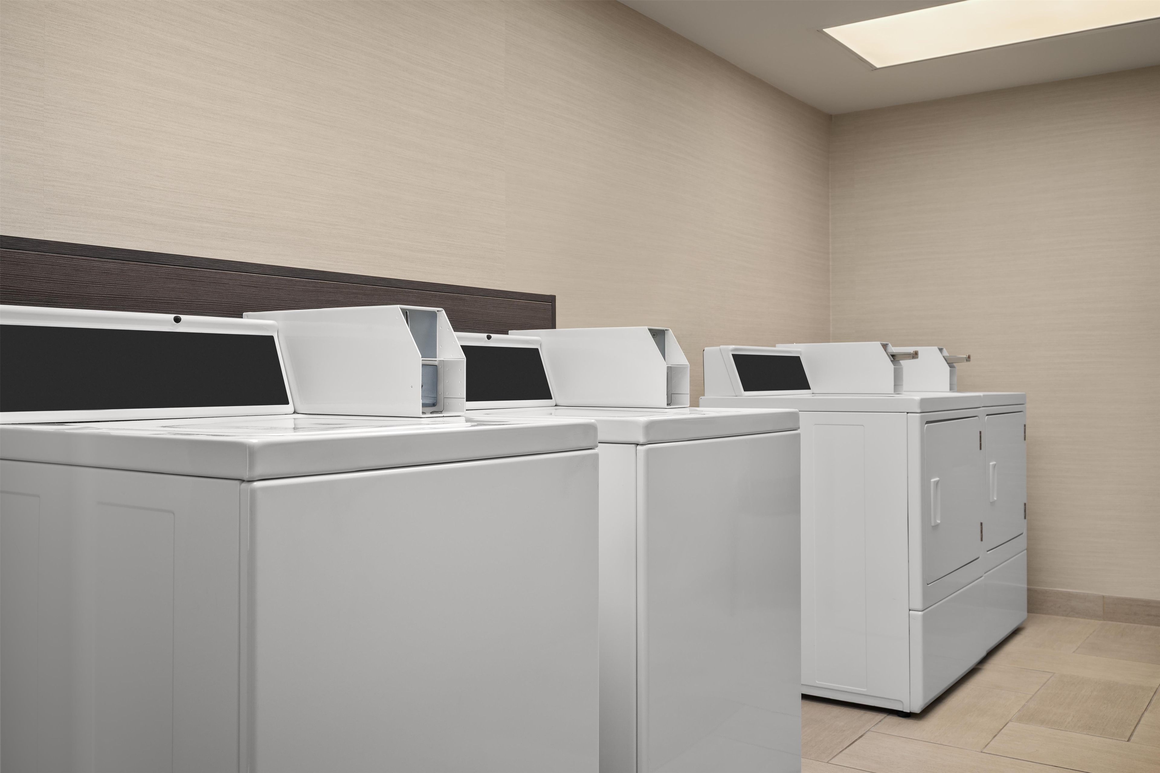 A laundry room with three front-loading washing machines and a dryer.