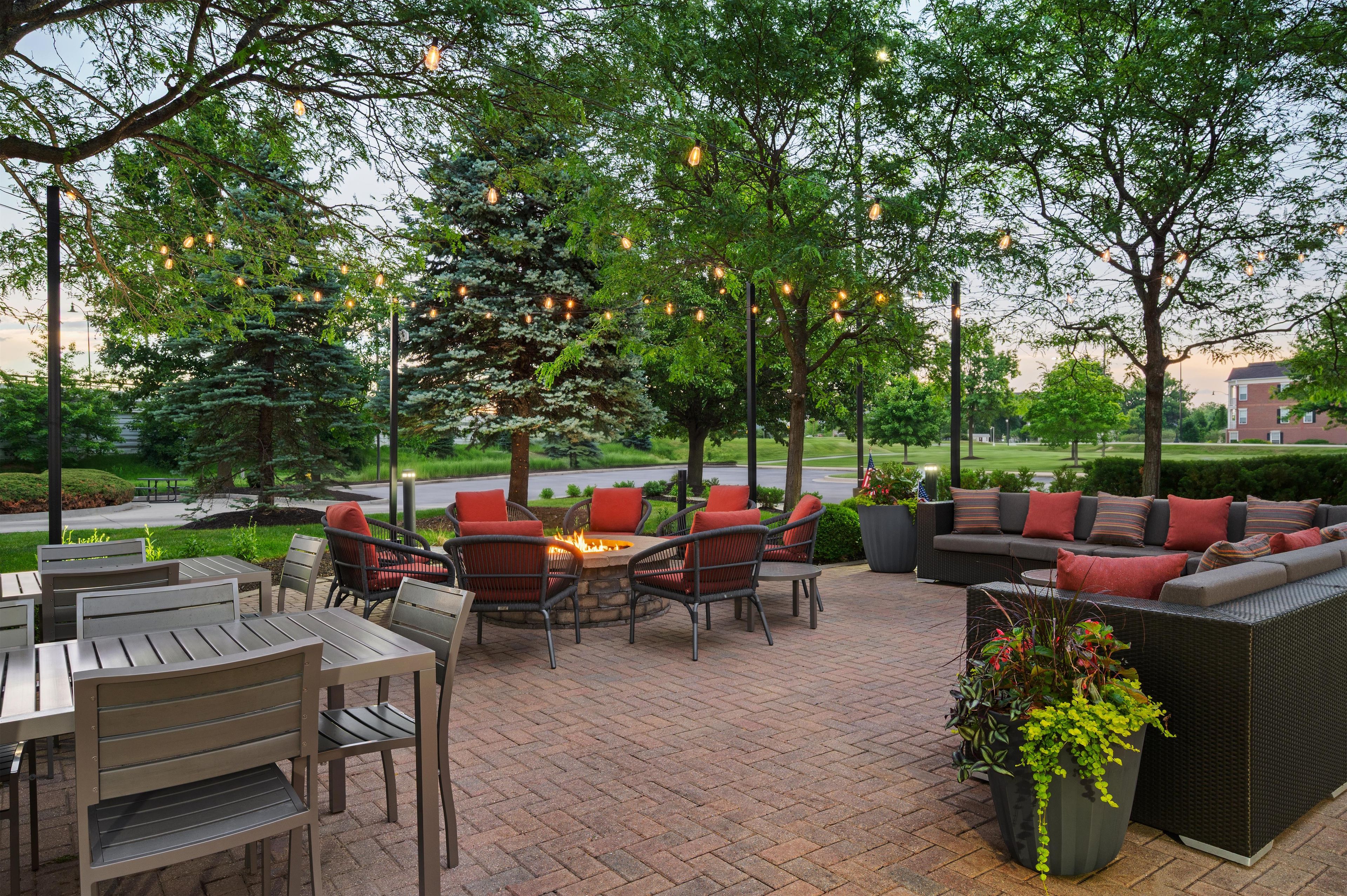 An outdoor patio area with seating arrangements, including chairs and a sofa, surrounded by trees and string lights.
