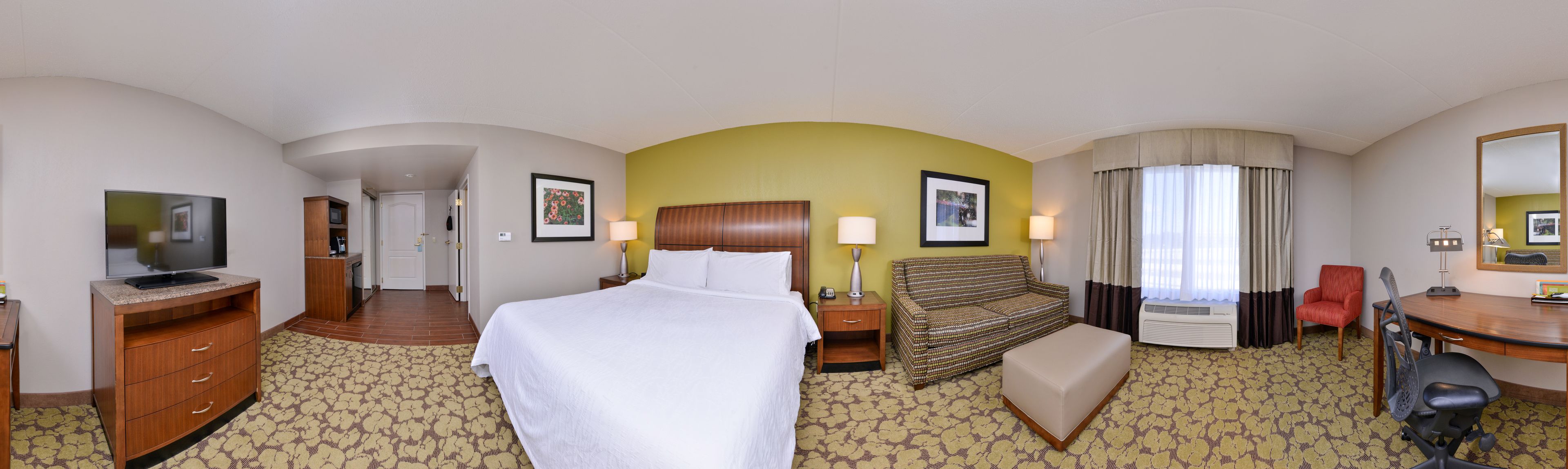 A hotel room with a bed, a desk, a chair, a TV, a sofa, and a bathroom.
