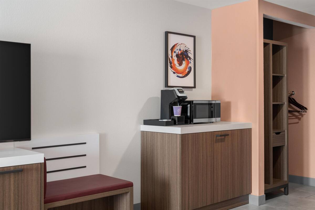 A reception desk with a coffee machine, a framed artwork, a television, and a wooden cabinet.