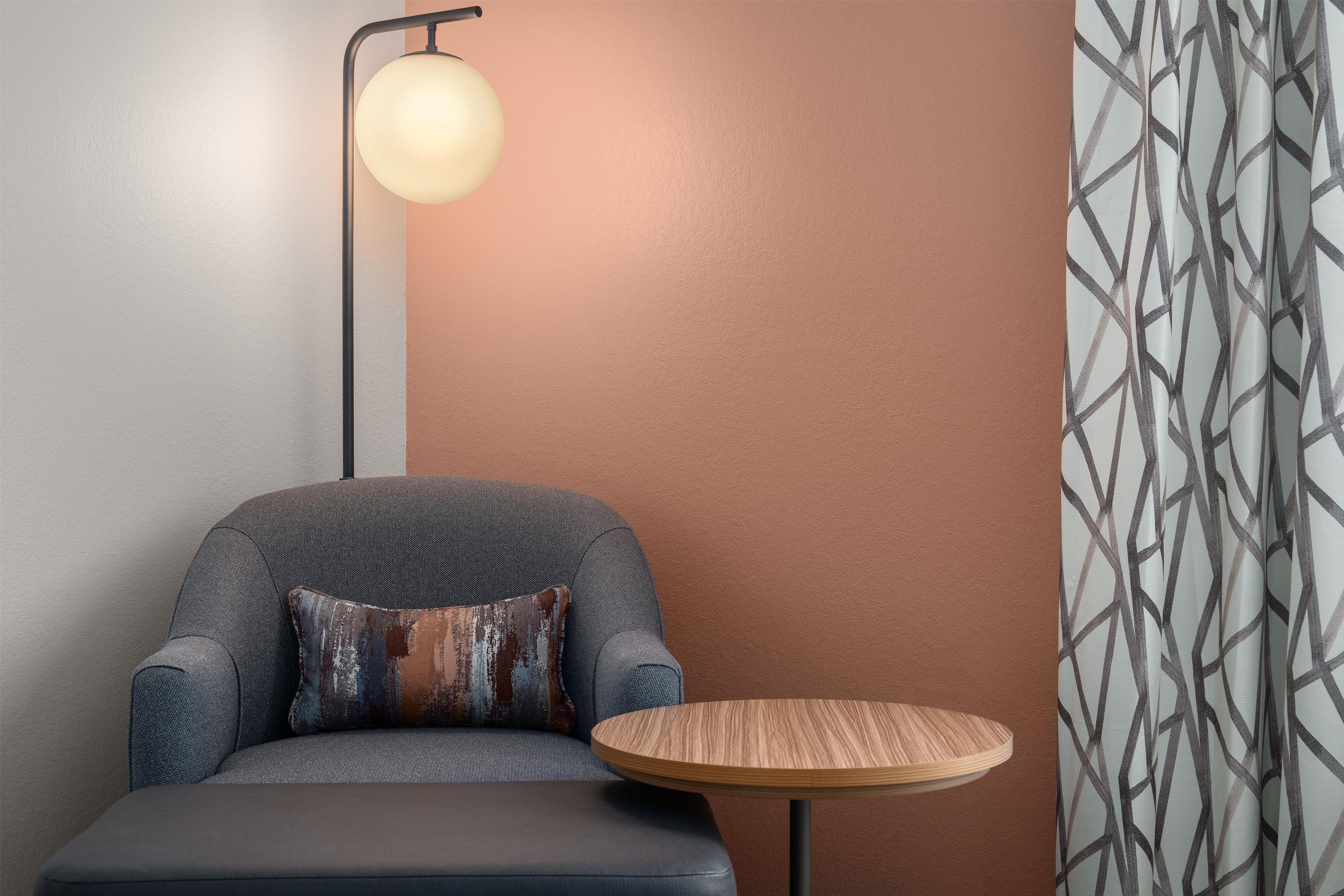 A room with a sofa, a round wooden table, a floor lamp, and a patterned wall.
