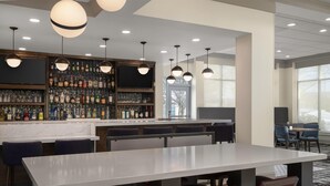 A bar area with a long counter, multiple hanging pendant lights, and a variety of liquor bottles.