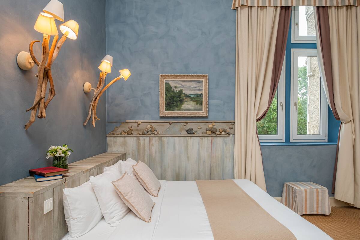 A bedroom with a bed, bedside tables, a nightstand, a framed picture, and a window with curtains.