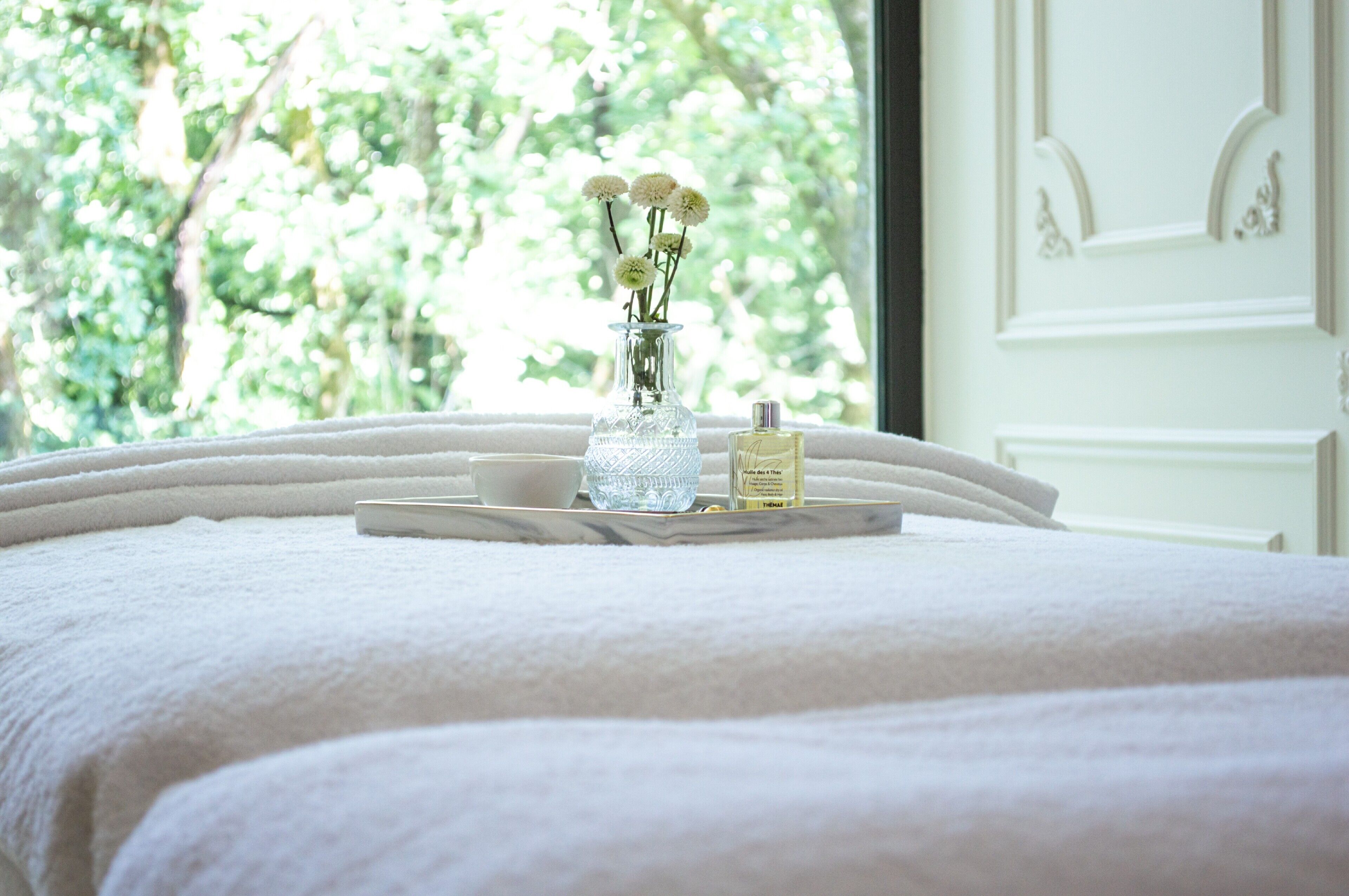 A bed with a tray holding a vase of flowers, a bottle of perfume, and a small bowl.