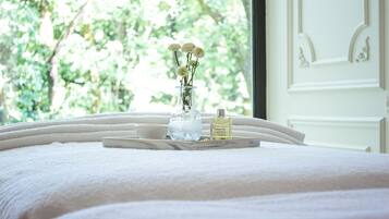 A bed with a tray holding a vase of flowers, a bottle of perfume, and a small bowl.