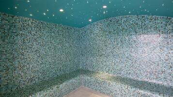 A room with a mosaic tiled wall and ceiling, a bench, and recessed lighting.