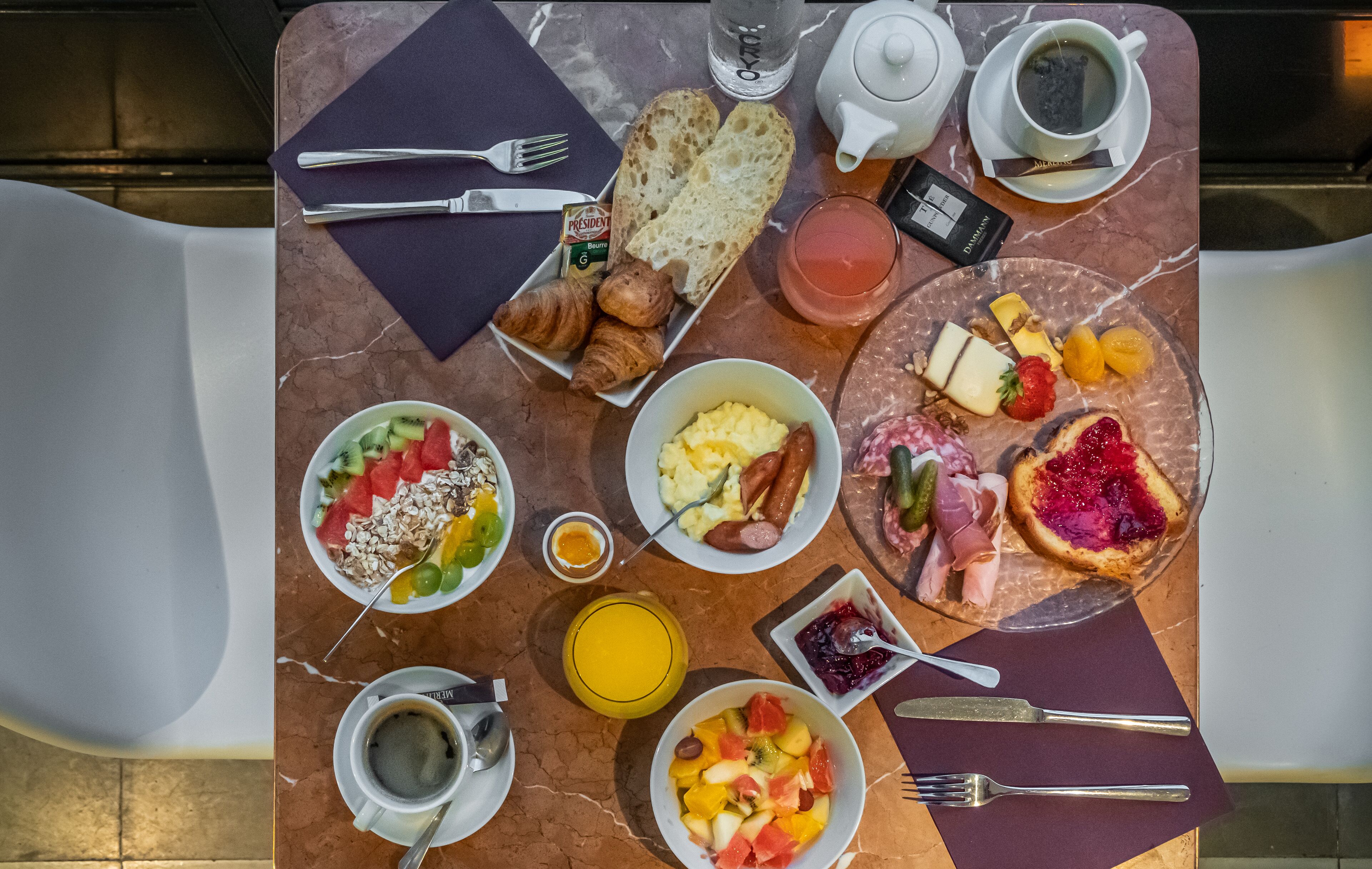 Aamiaispöydässä on croissantteja, hedelmiä, munakokkelia, makkaroita ja erilaisia levitteitä.