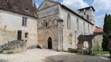 A historic stone building with a central arched entrance, a bell tower, and a small staircase leading to a door.