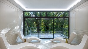 Ein modernes Interieur mit weißen, geschwungenen Stühlen, einem Glasbalkon und Blick ins Grüne.