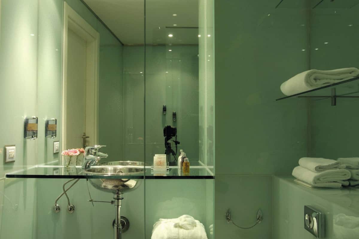 Un bagno moderno con un lavandino in vetro, cabina doccia in vetro e un appendi-asciugamani.