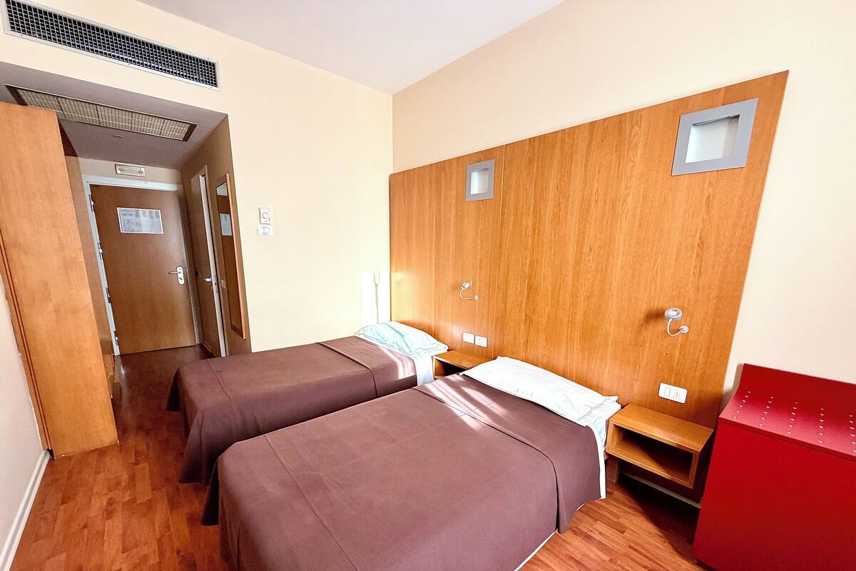 Una camera d'albergo con due letti, pannelli di legno sulle pareti, un armadietto rosso e pavimento in legno.