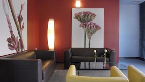 Un vestíbul modern amb un sofà de pell negra, un butaquesa groc i una taula de cafè de vidre amb un ram de flors.