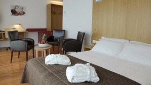 Habitació d'hotel amb llit, dues cadires, una taula petita i un quadre a la paret.