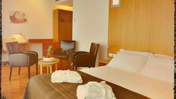 A hotel room with a bed, two chairs, a small table with a fruit bowl, and a lamp.