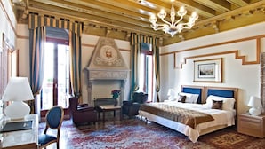 Una habitación de hotel con una cama grande, una chimenea, un escritorio con lámpara y una silla.