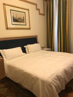 Una camera d'albergo con un letto rifatto, un quadro appeso al muro e una tenda a righe.