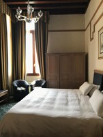 Una camera d'albergo con un letto grande, due poltrone, un guardaroba in legno e un lampadario.
