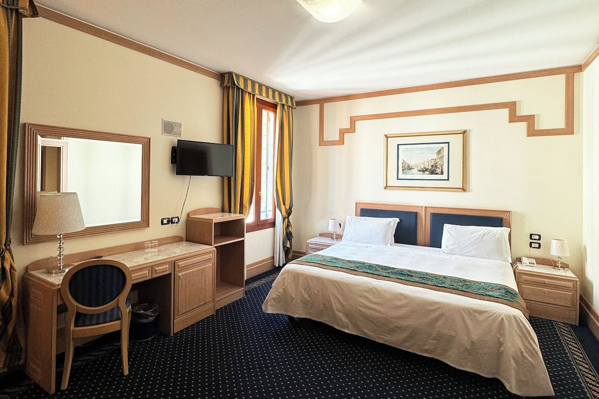 A hotel room with a bed, desk, chair, and a television.
