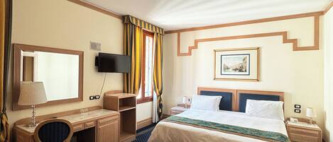 A hotel room with a bed, desk, chair, and a television.