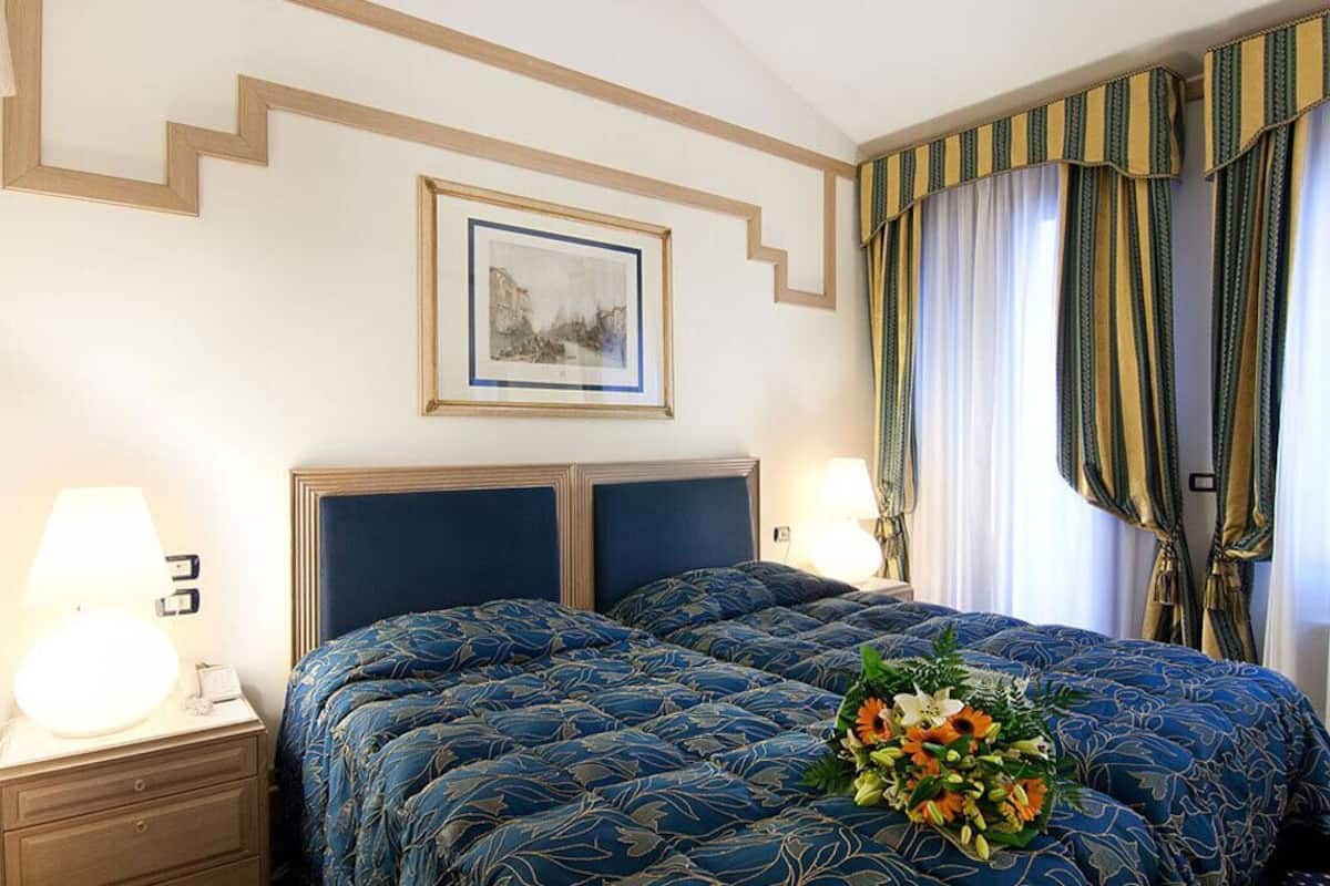 A hotel room with a large bed, two bedside tables, a framed picture on the wall, and curtains.