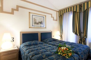 Una camera d'albergo con un letto grande, due comodini, un quadro appeso e tende.