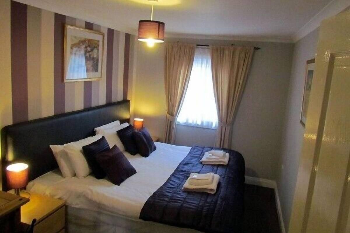 A hotel room with a large bed, striped walls, a framed picture, a window with curtains, and a nightstand with a lamp.