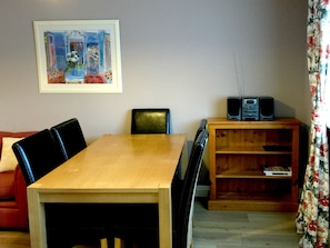 A room with a wooden dining table, black chairs, a red sofa, a wooden bookshelf, and a framed painting on the wall.