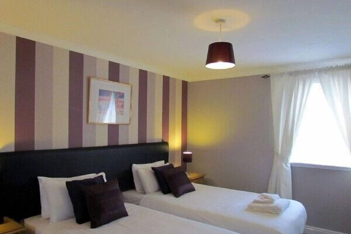 A hotel room with two beds, striped wallpaper, a framed picture on the wall, and a window with curtains.