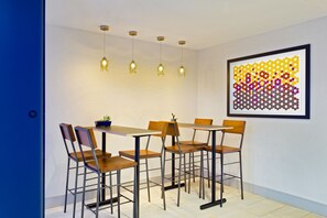 Uma área de refeições com mesa e cadeiras, luminárias pendentes e uma obra de arte abstrata emoldurada na parede.