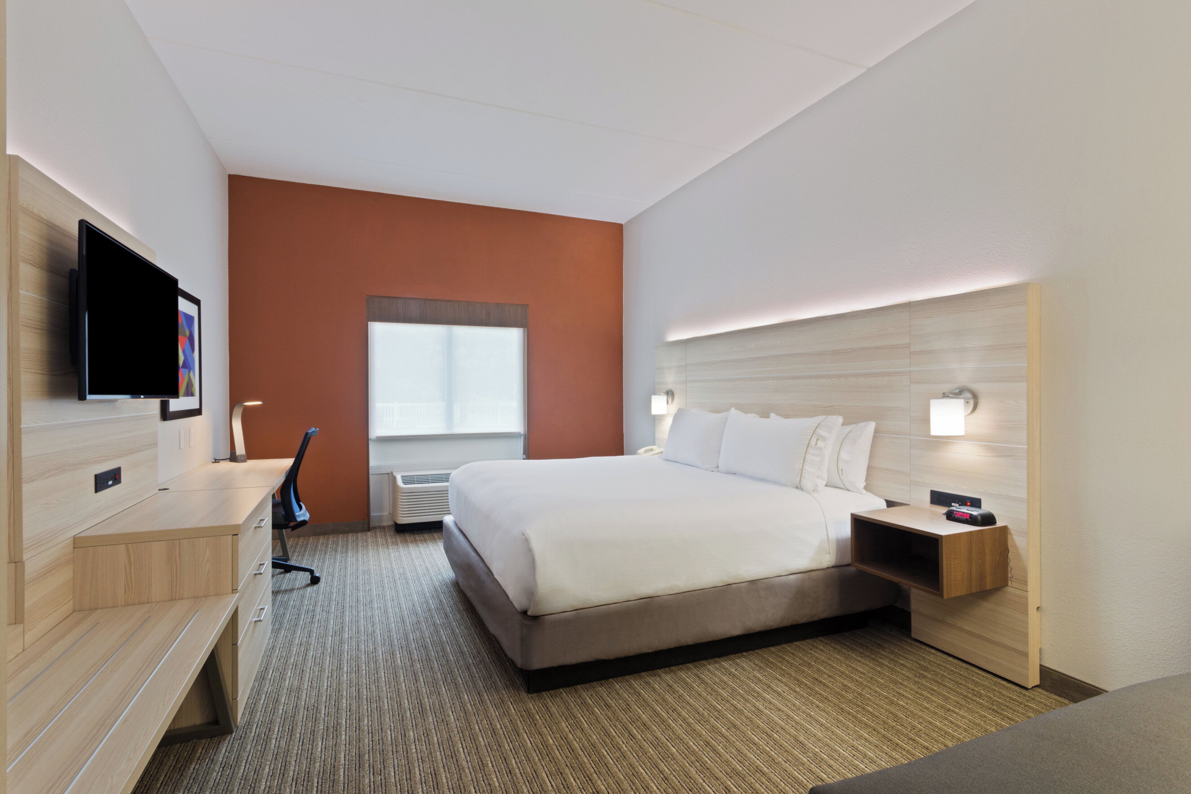 A hotel room with a bed, bedside table, desk, chair, and a flat-screen TV.