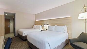 A hotel room with two beds, a desk, a chair, a lamp, and a phone on the nightstand.
