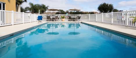 Piscina con cerca blanca, sillas de descanso y sombrillas.