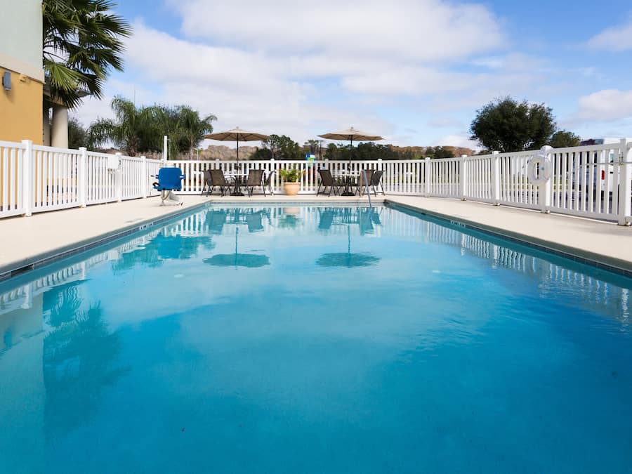 A swimming pool with a white fence, lounge chairs, and umbrellas.