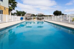 Piscina cercada por grade branca, com espreguiçadeiras e guarda-sóis.