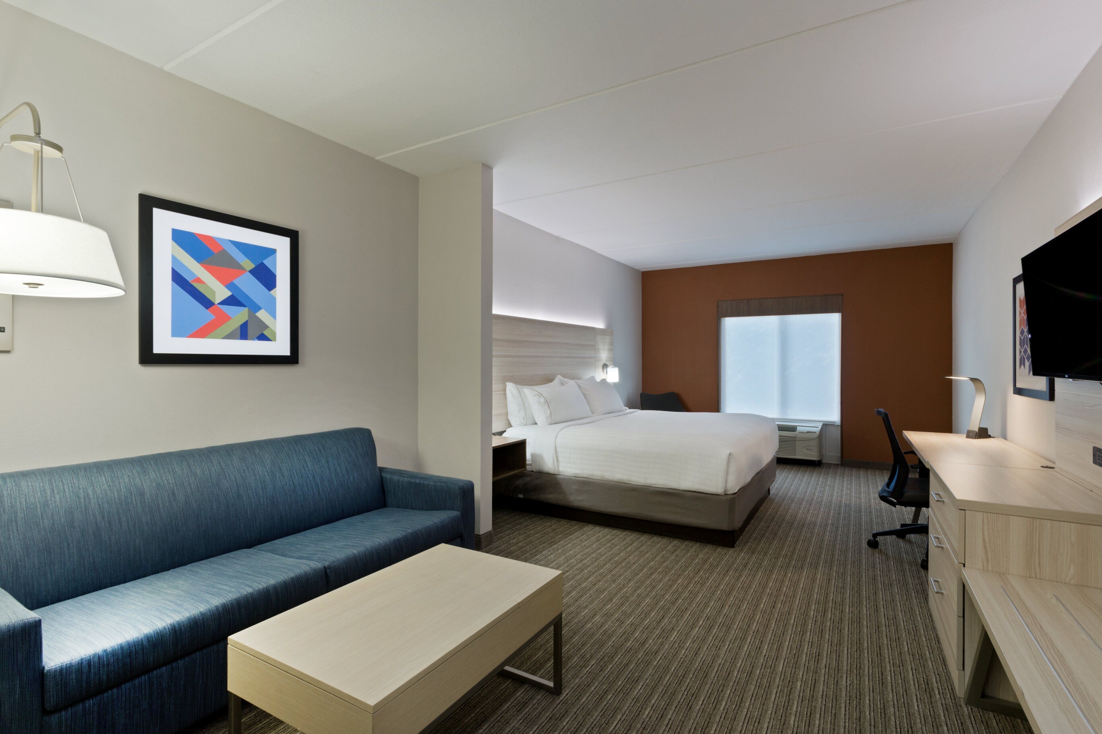 A hotel room with a bed, a sofa, a desk, and a TV.