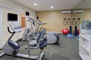 Uma sala de ginástica equipada com esteiras, elíptica, bolas de exercício e dispensador de água.