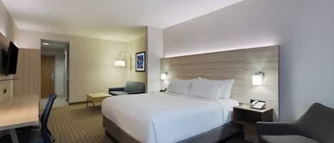 A hotel room with a bed, desk, chair, bedside table, and a flat-screen TV.