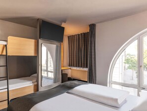 Een compacte hotelkamer met een stapelbed, een klein bureau en een groot raam met uitzicht.