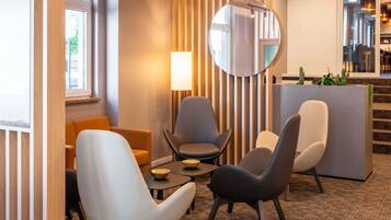 Un hall d’hôtel moderne avec un espace salon, un grand miroir rond et un escalier menant à un étage supérieur.