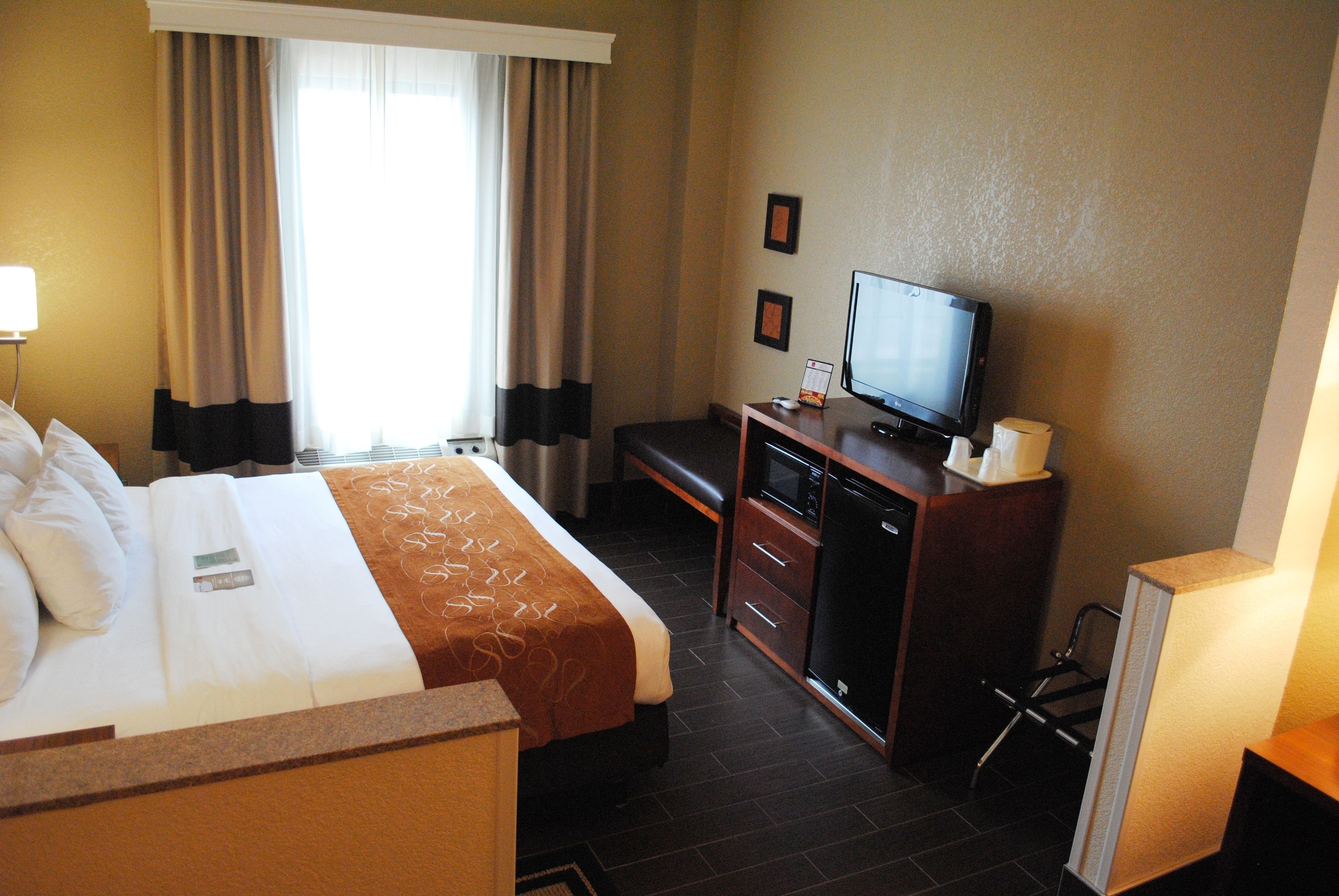 A hotel room with a bed, a desk with a television, a desk lamp, and a chair.