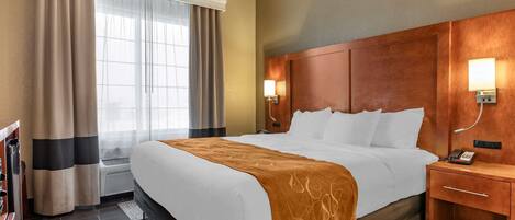 A hotel room with a large bed, a wooden headboard, a bedside table with a lamp, and a window with curtains.