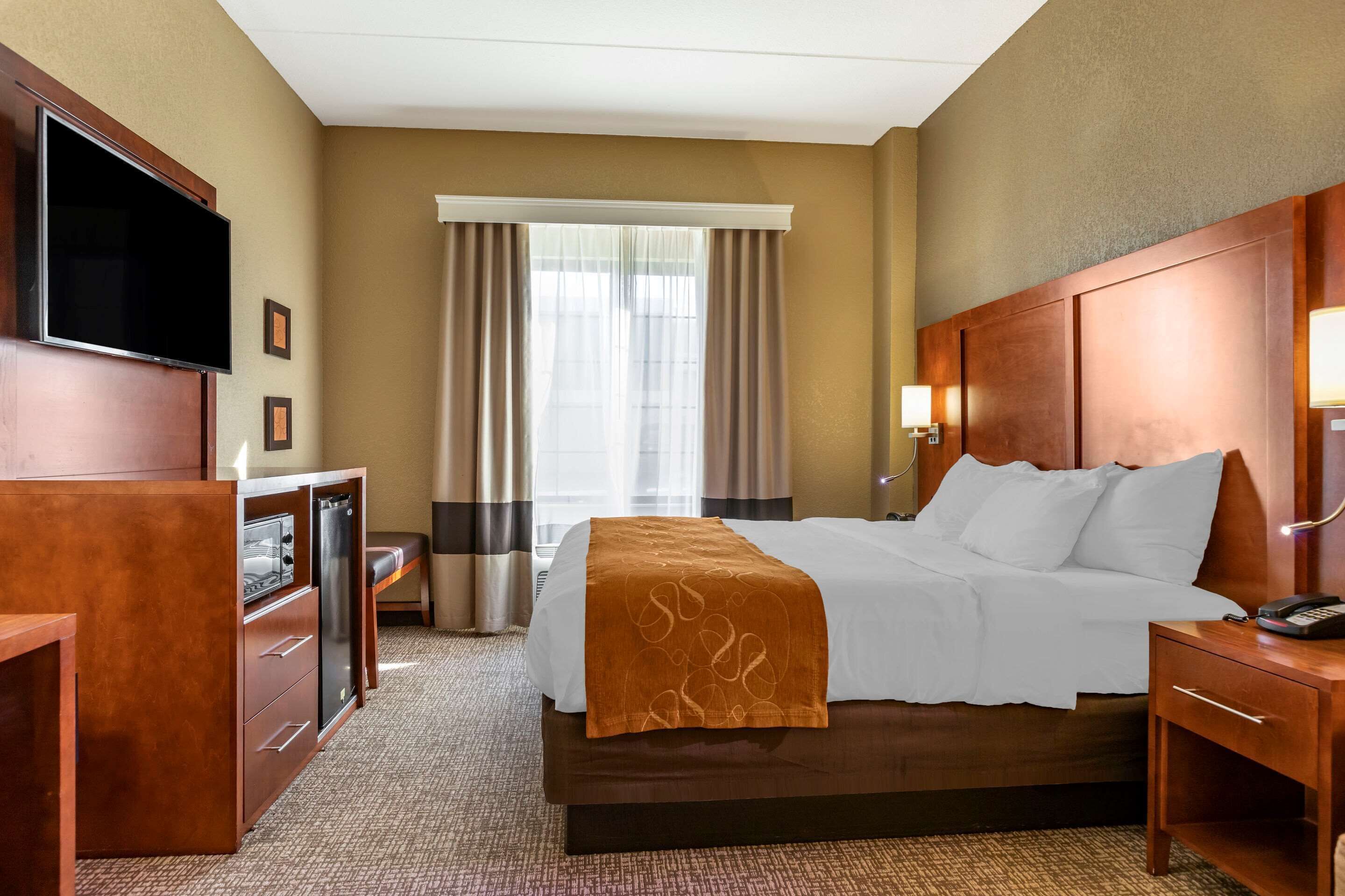 Une chambre d’hôtel avec un lit, une télévision, un bureau et une fenêtre avec des rideaux.