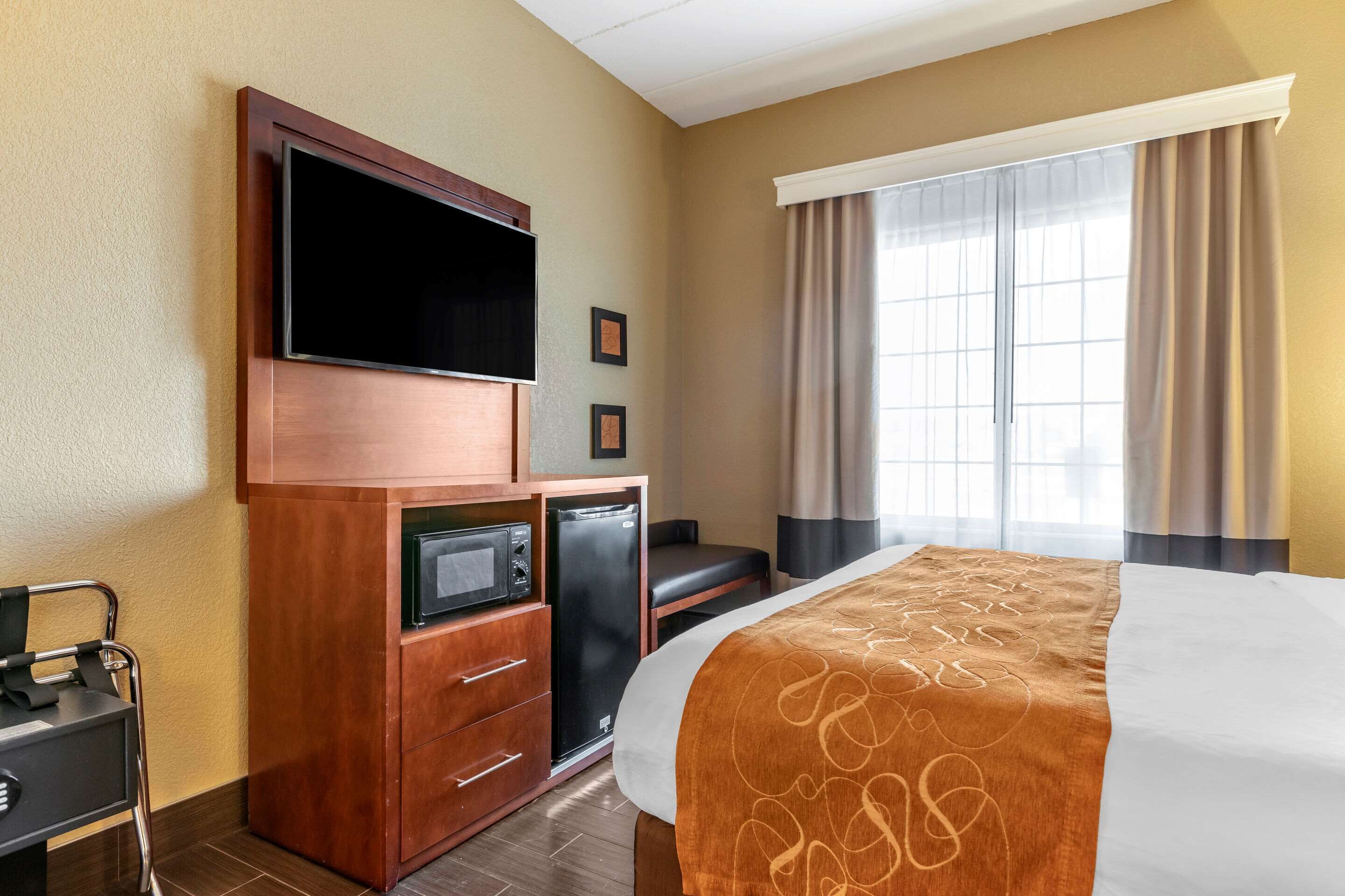 Una camera d'albergo con un letto, una TV, un mini-frigo, un forno a microonde e una scrivania con una sedia.