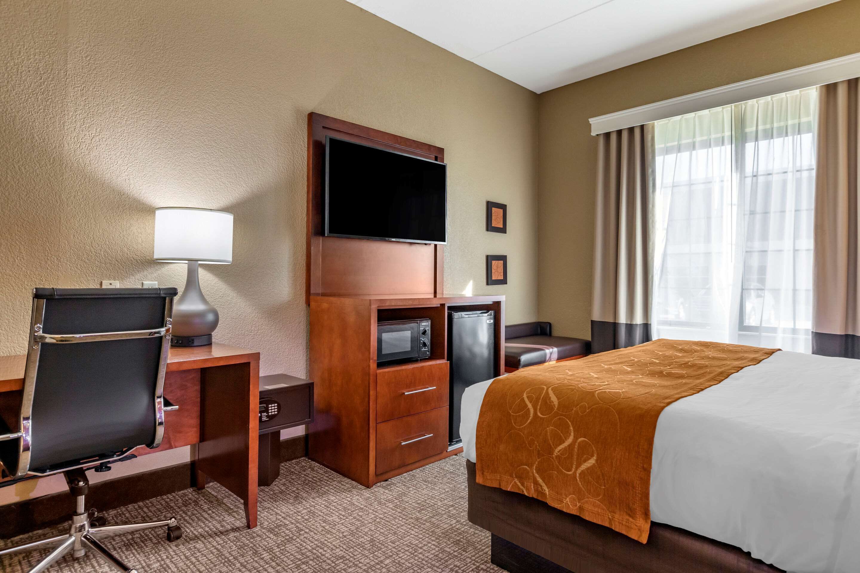 Habitación de hotel con cama, escritorio con silla, televisión, microondas, refrigerador y ventana con cortinas.