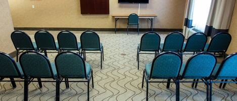 Un salón de conferencias con filas de sillas verdes, una televisión de pantalla plana, una mesa de madera y una alfombra estampada.