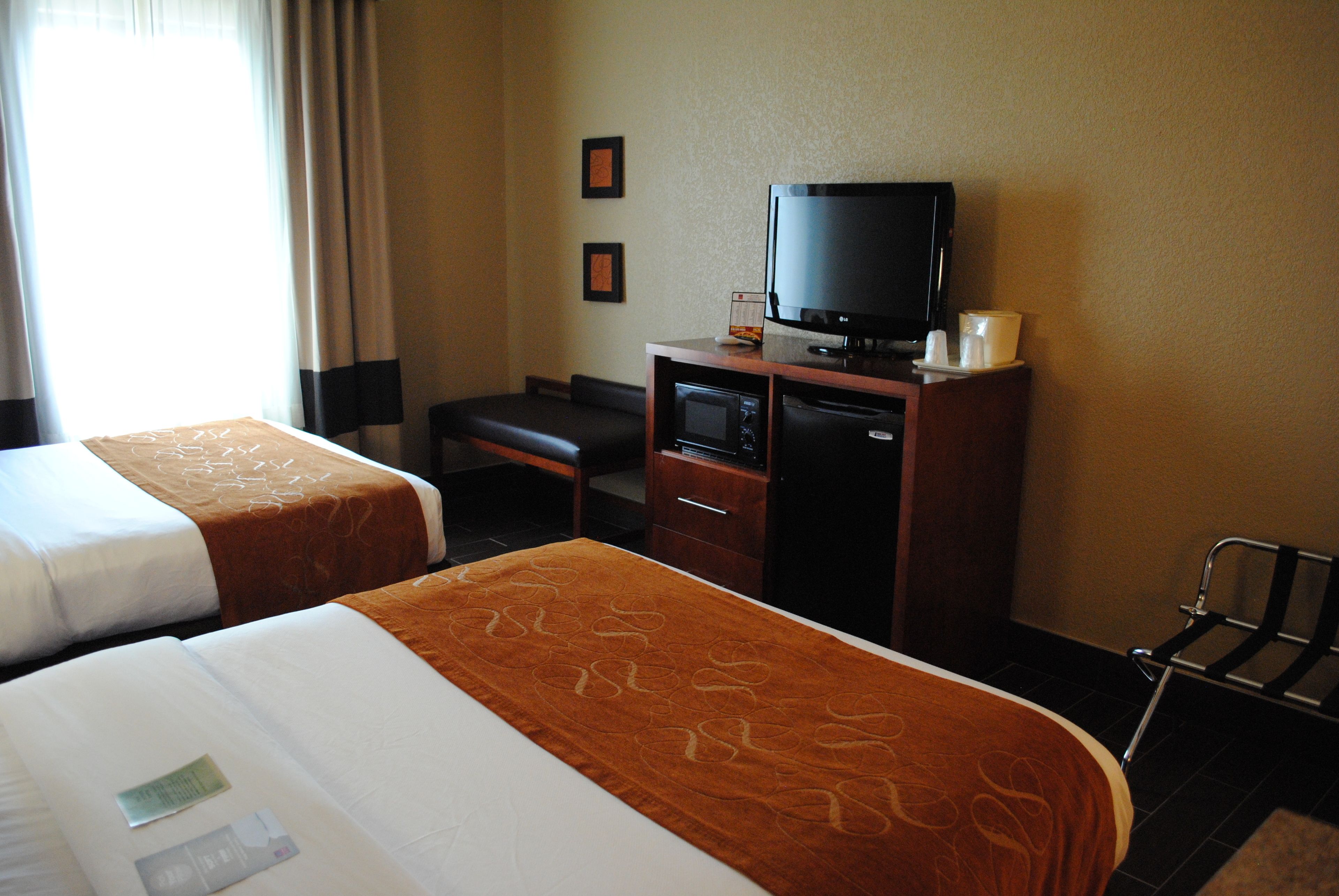 A hotel room with two beds, a television, a desk, and a chair.