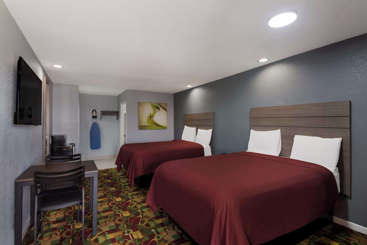 A hotel room with two beds, a desk, a chair, a TV, and a patterned carpet.